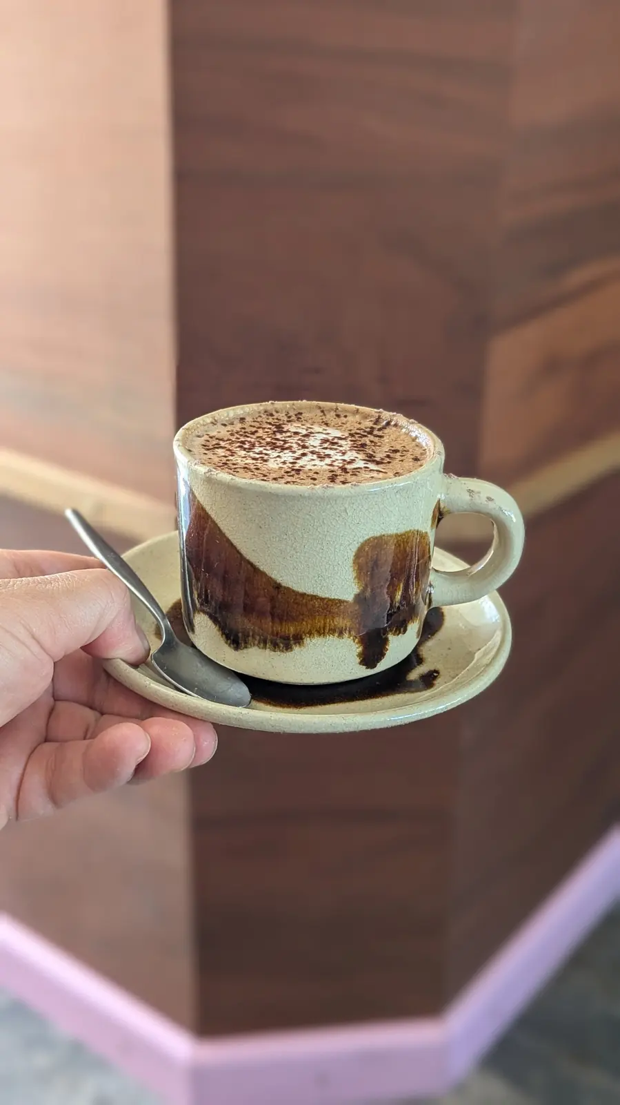 Hot chocolate in a handmade cup, with a pink skirting board behind it.