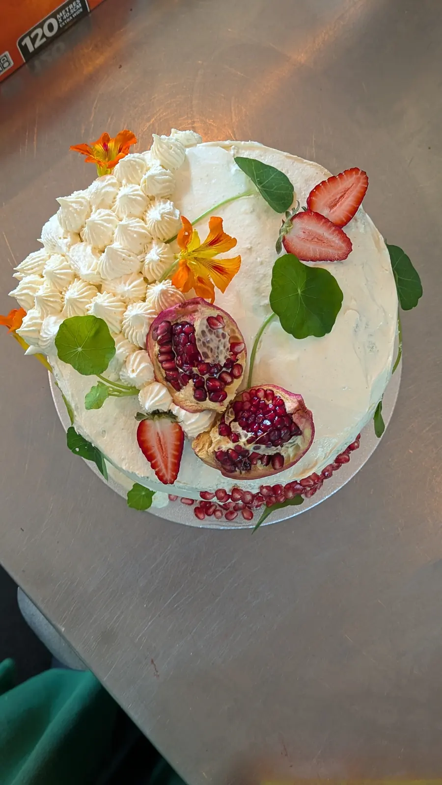 A white celebration cake with flowers, strawberries and pomegranate.