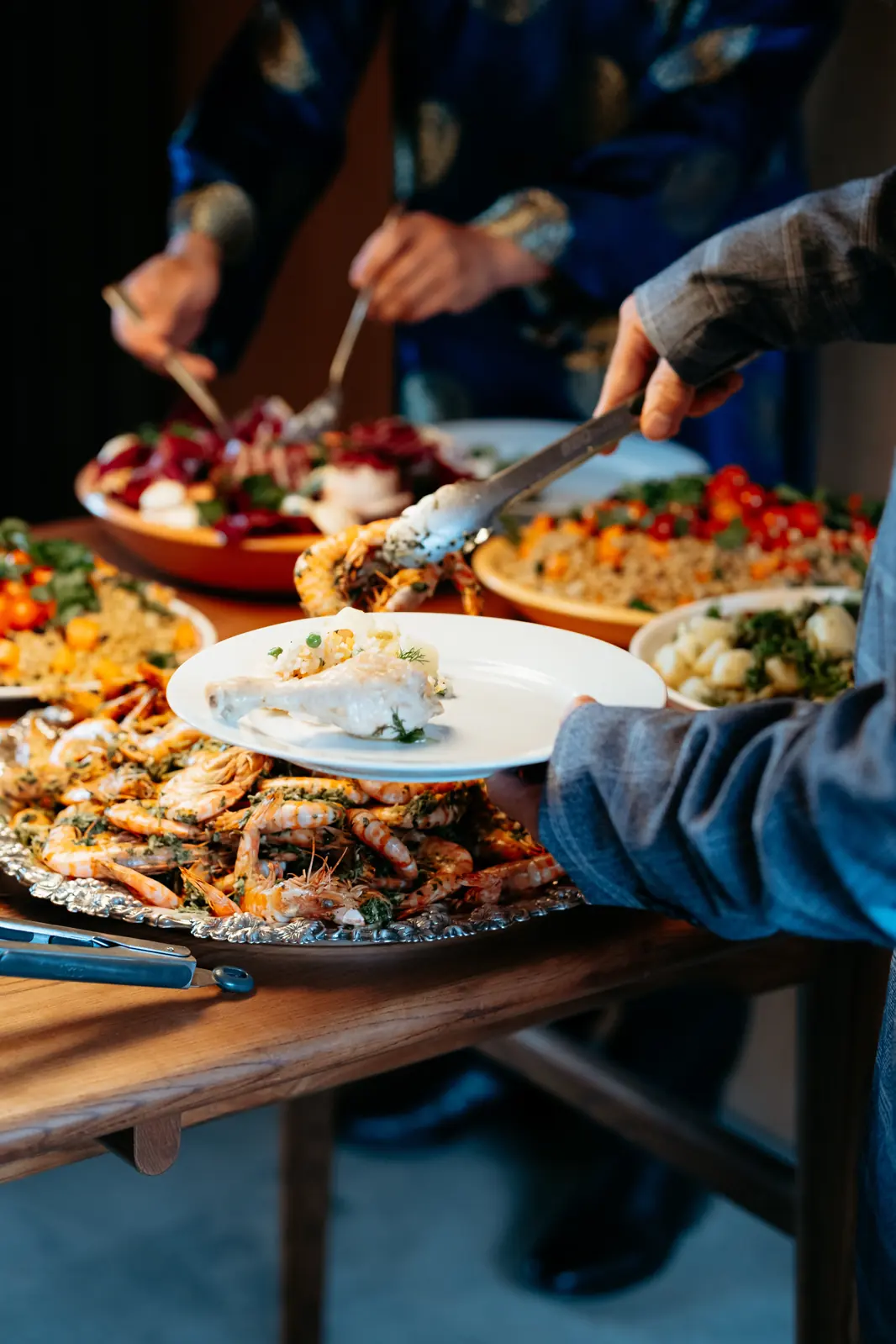 Hands serving from a large grazing platter of salads, bread and roasted vegetables.