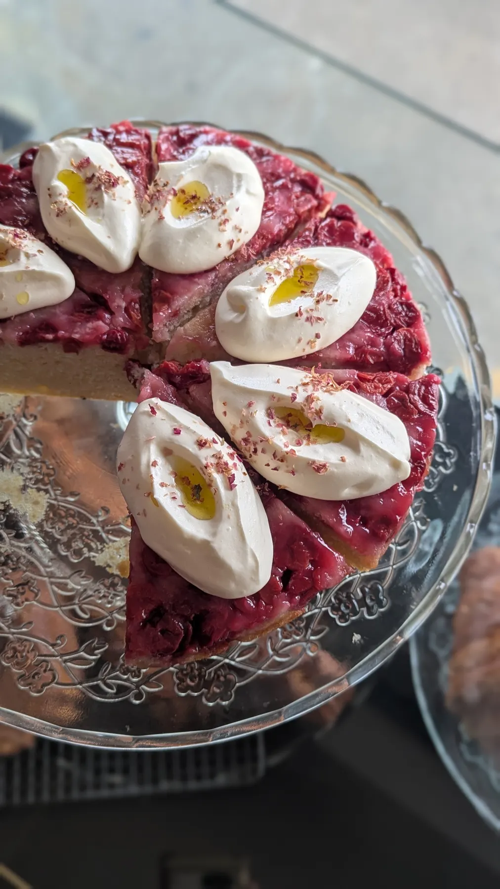 A berry cake with cream, sliced on a glass stand.